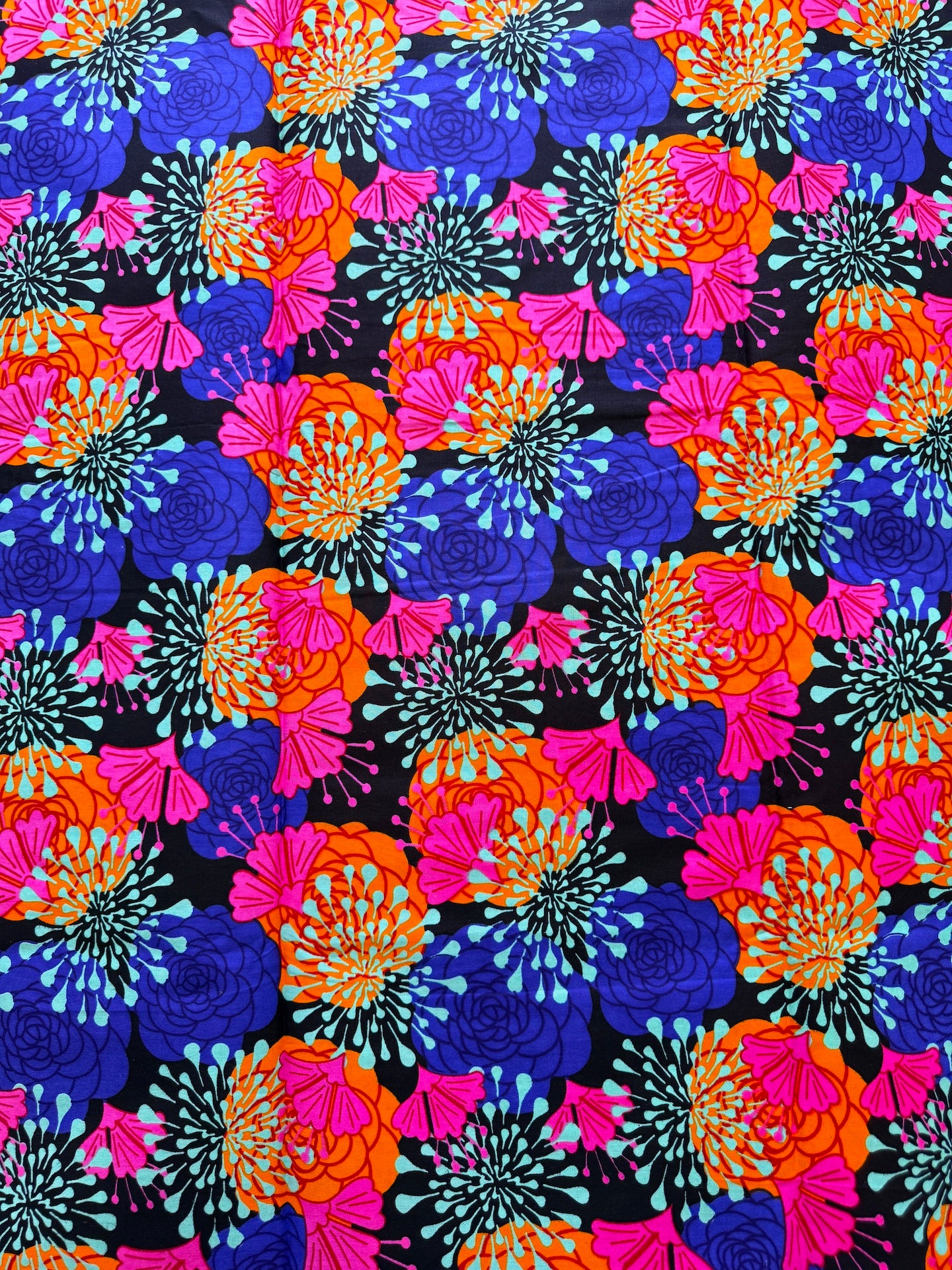 A vibrant, repeating floral pattern featuring stylized flowers in bright pink, orange, and royal blue on a black background.