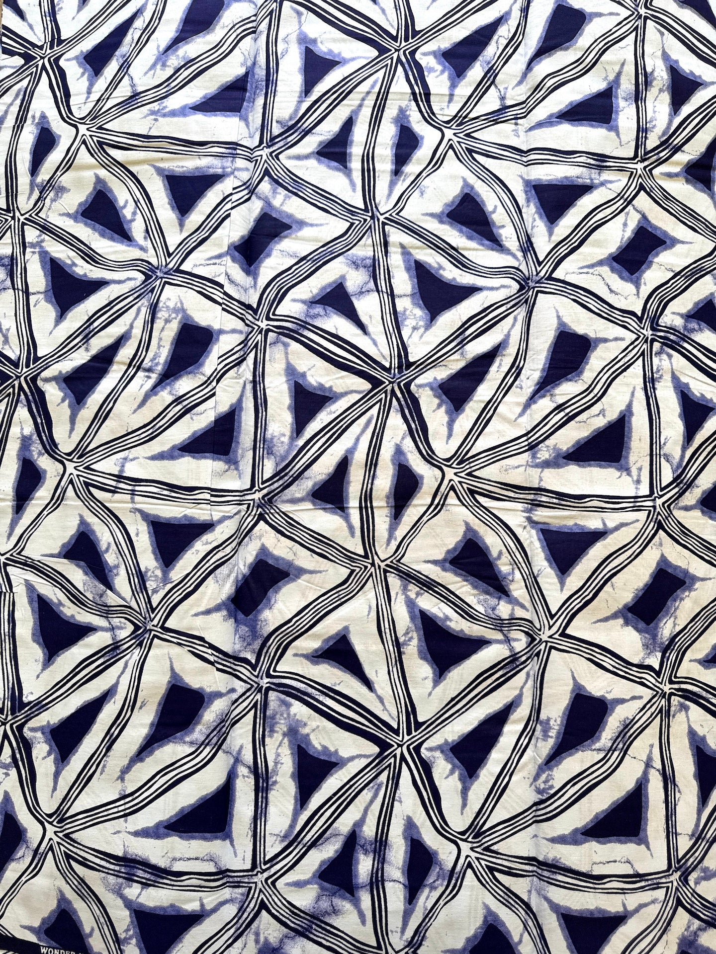 A close-up of a batik fabric with a repeating geometric pattern of interlocking triangles and diamonds in navy blue, cream, and black.