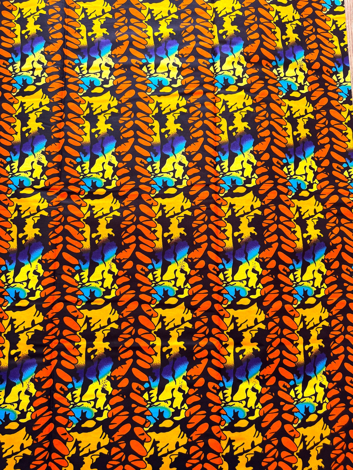 A close-up of a vibrant fabric or wallpaper pattern featuring vertical columns of orange and yellow leaf-like motifs over a black background with bright blue and yellow abstract accents.