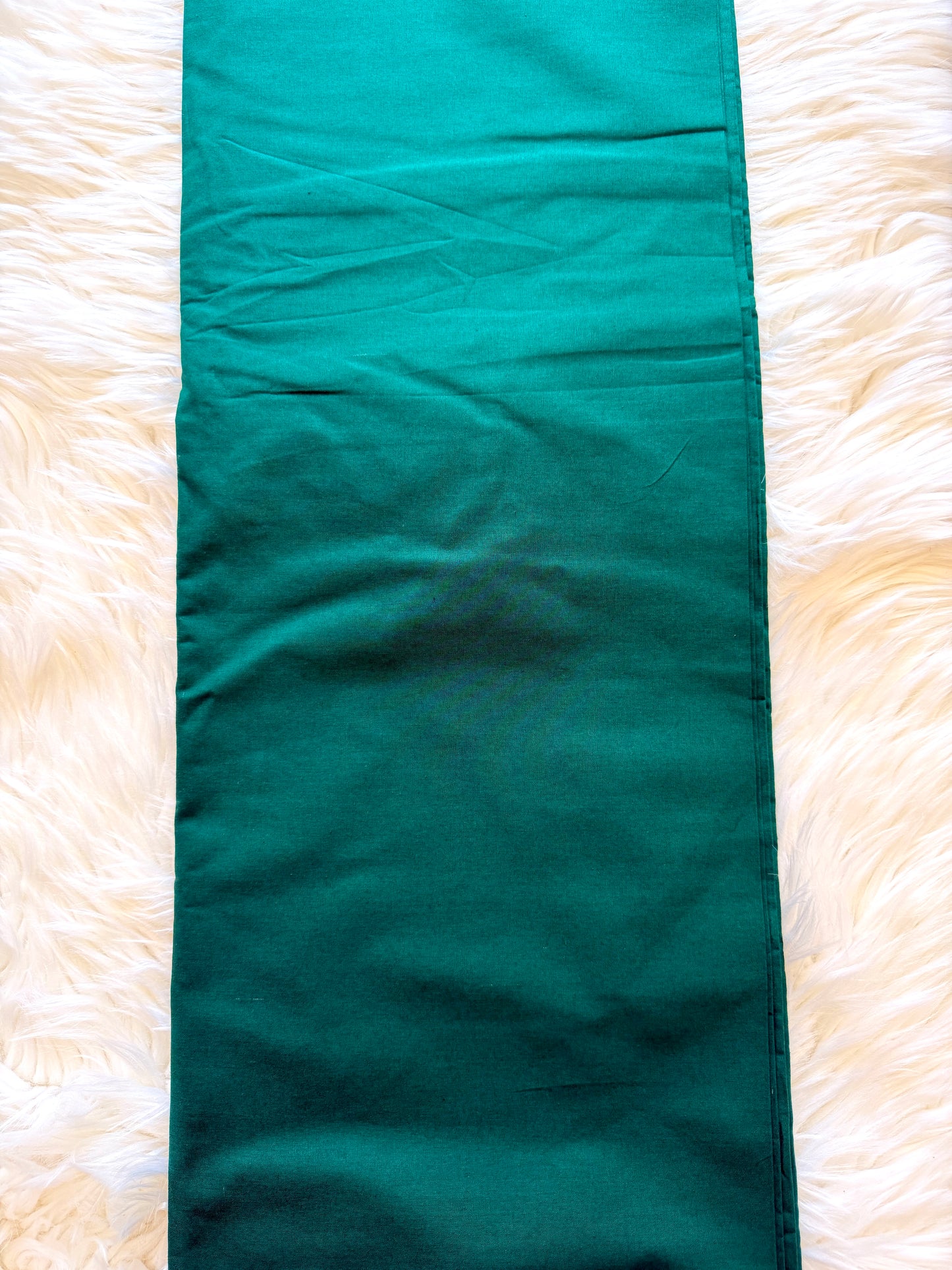 A long, narrow teal-green fabric runner or table runner laid flat on a white faux fur surface.