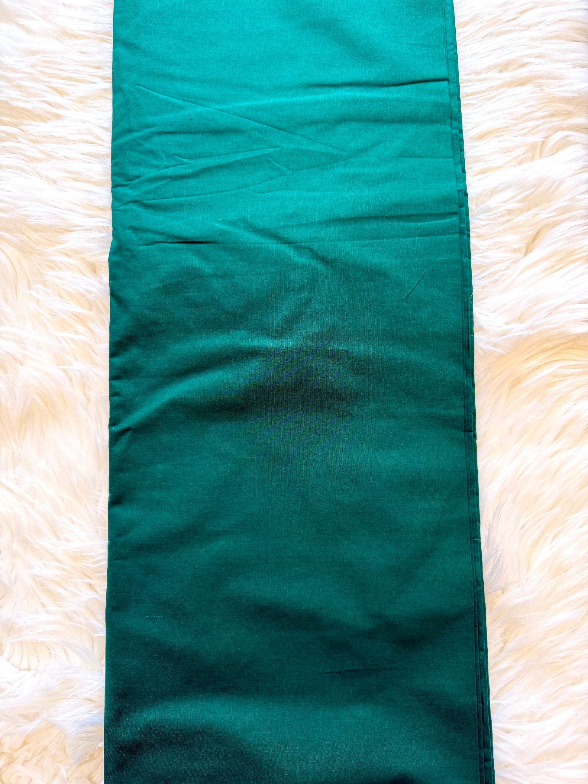 A long, narrow teal-green fabric runner or table runner laid flat on a white faux fur surface.