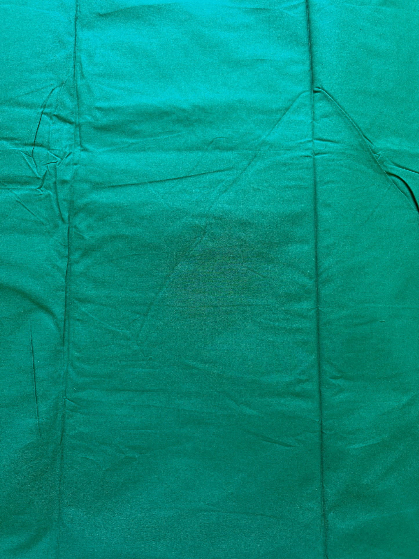 A close-up of a teal green fabric surface with visible folds, seams, and slight wrinkling.