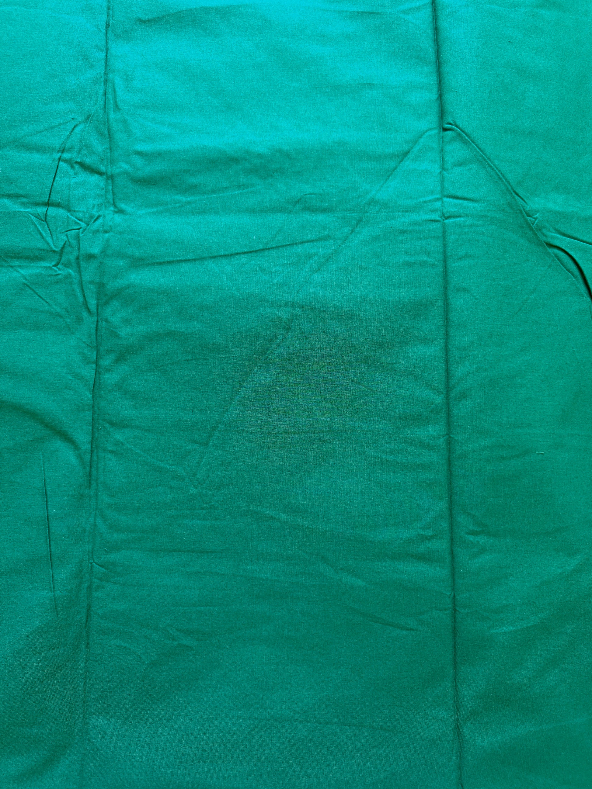 A close-up of a teal green fabric surface with visible folds, seams, and slight wrinkling.