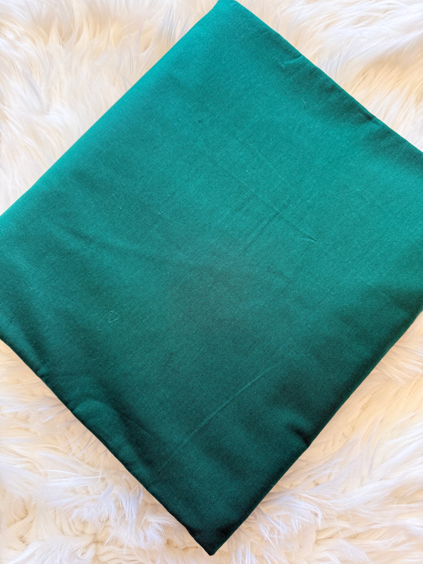 A teal green rectangular fabric cushion cover or pillow case laid flat on a white faux fur surface.