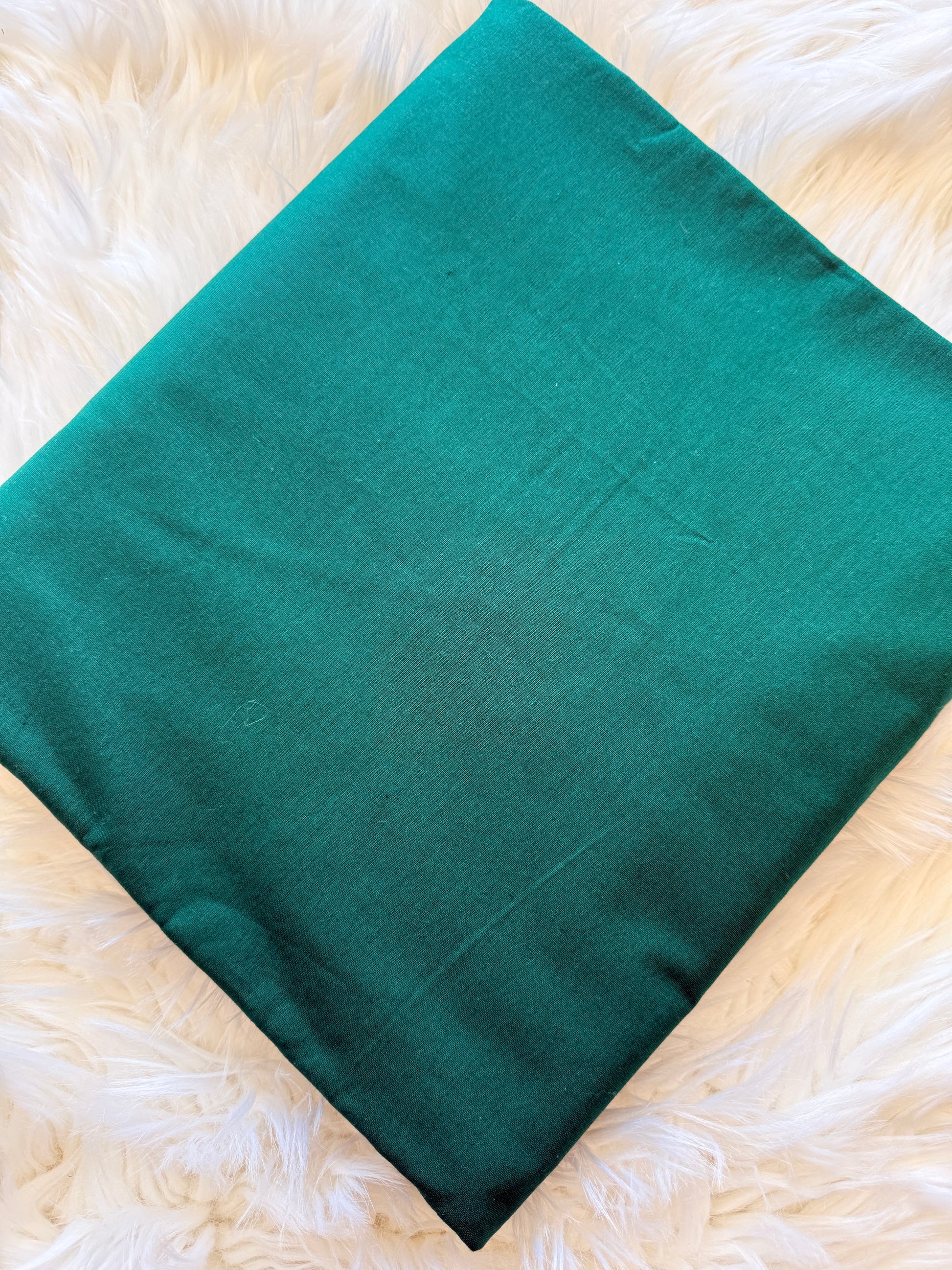A teal green rectangular fabric cushion cover or pillow case laid flat on a white faux fur surface.