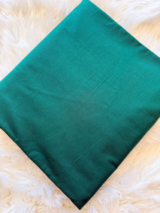 A teal green rectangular fabric cushion cover or pillow case laid flat on a white faux fur surface.