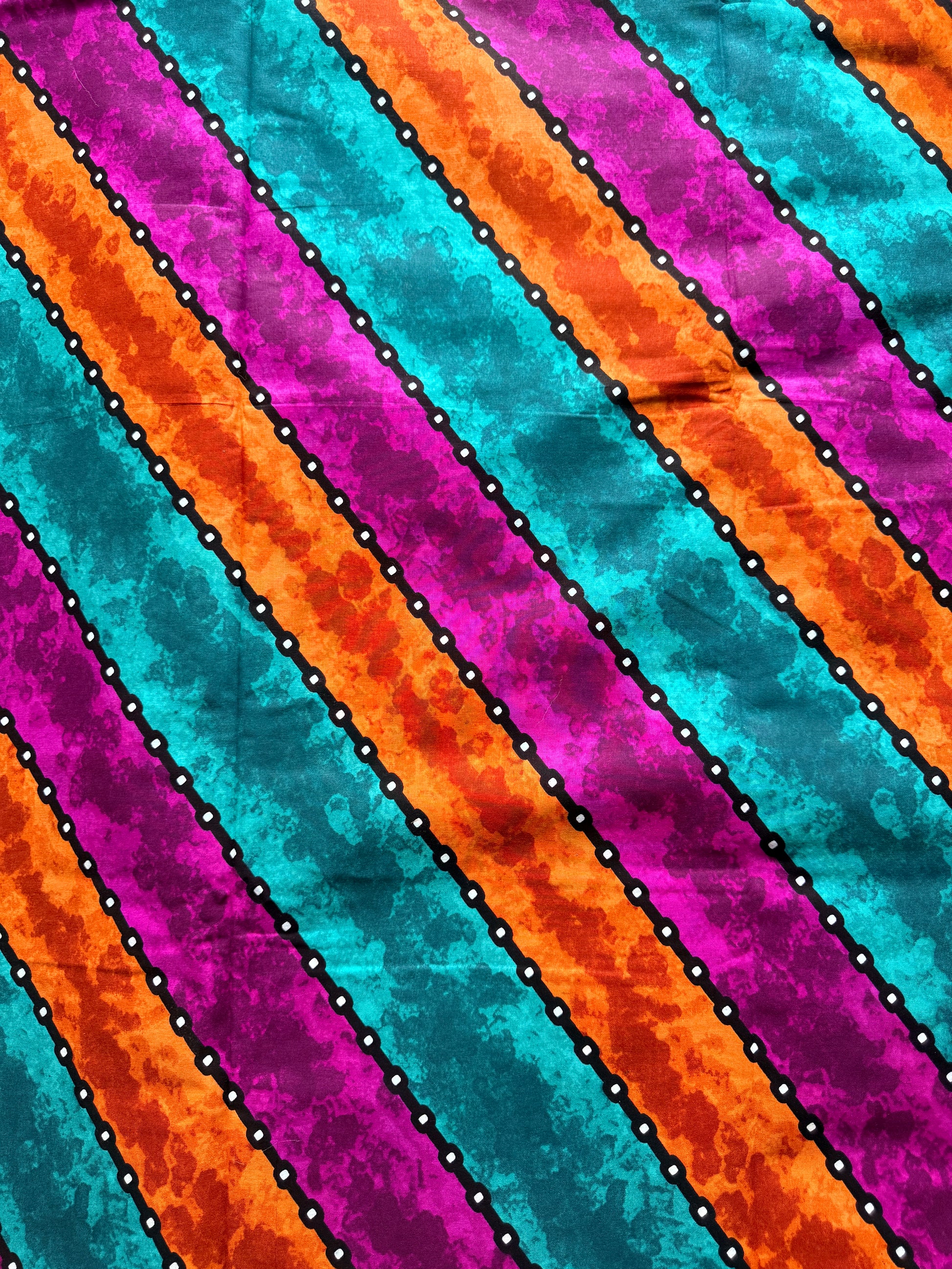 A close-up of a colorful striped fabric pattern with diagonal bands of turquoise, orange, magenta, and purple separated by black dotted lines with white dots.