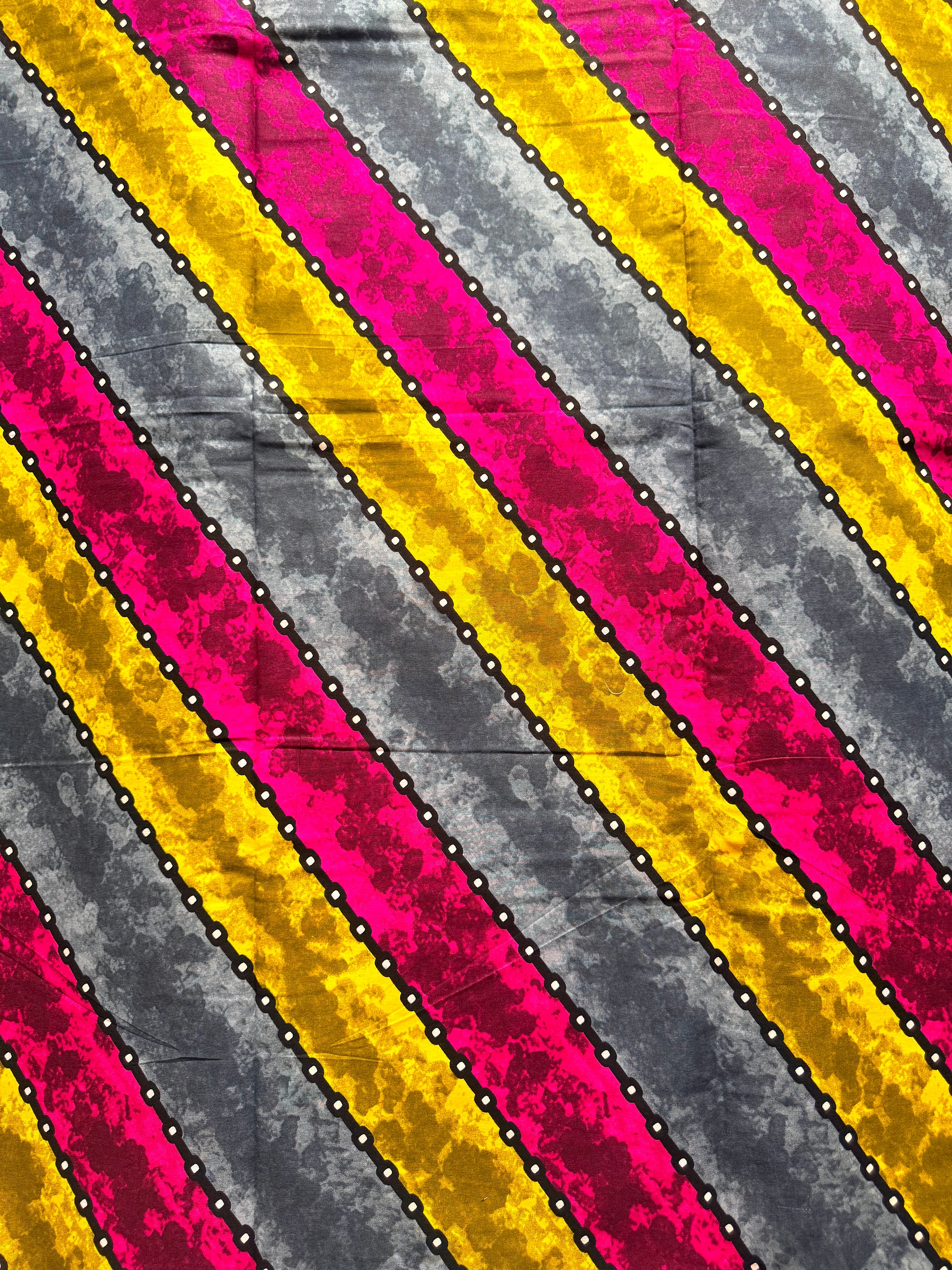 A close-up of a striped fabric pattern with diagonal bands of bright pink, yellow, and textured gray, separated by thin black and white dotted lines.