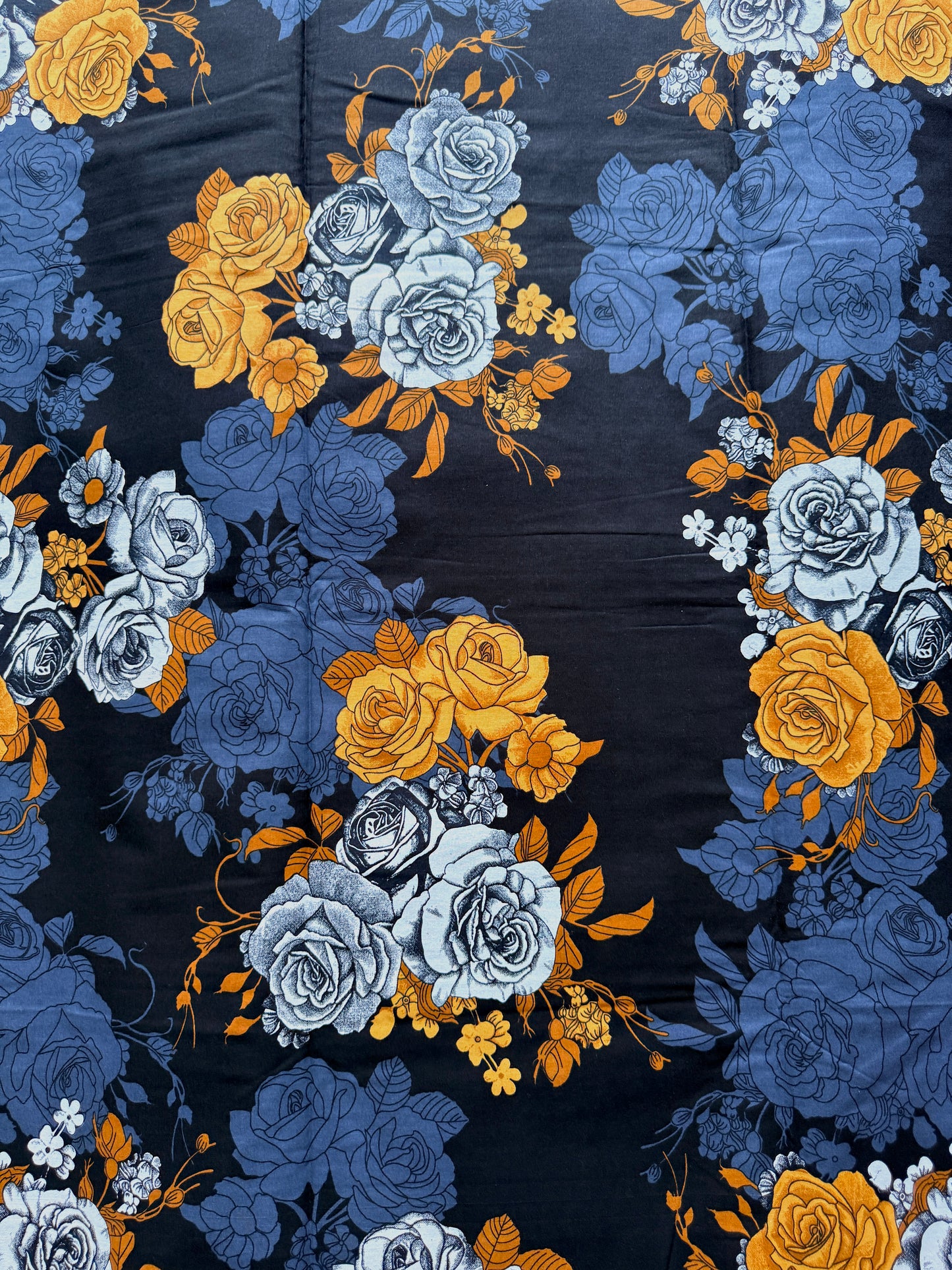 A close-up of a floral fabric pattern featuring blue and yellow roses on a dark navy background.