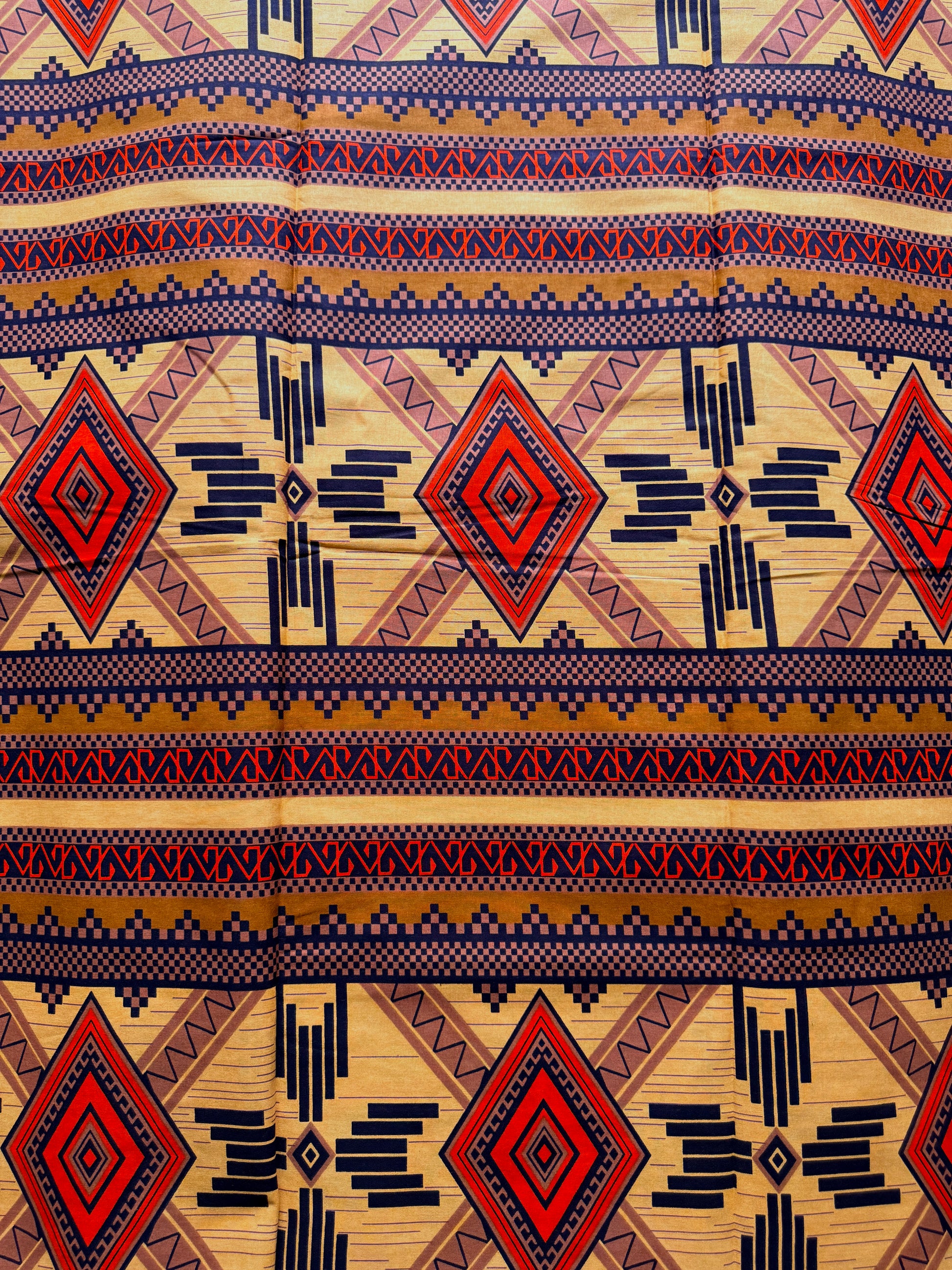 A close-up of a fabric with a Southwestern geometric pattern featuring red, navy blue, and beige stripes with diamond and zigzag motifs.