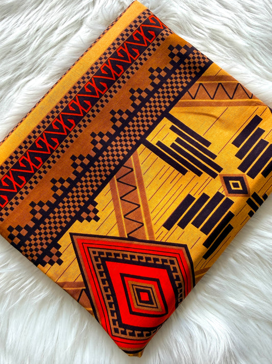 A folded textile with a bold geometric pattern in yellow, orange, red, and black, displayed on a white faux fur surface.