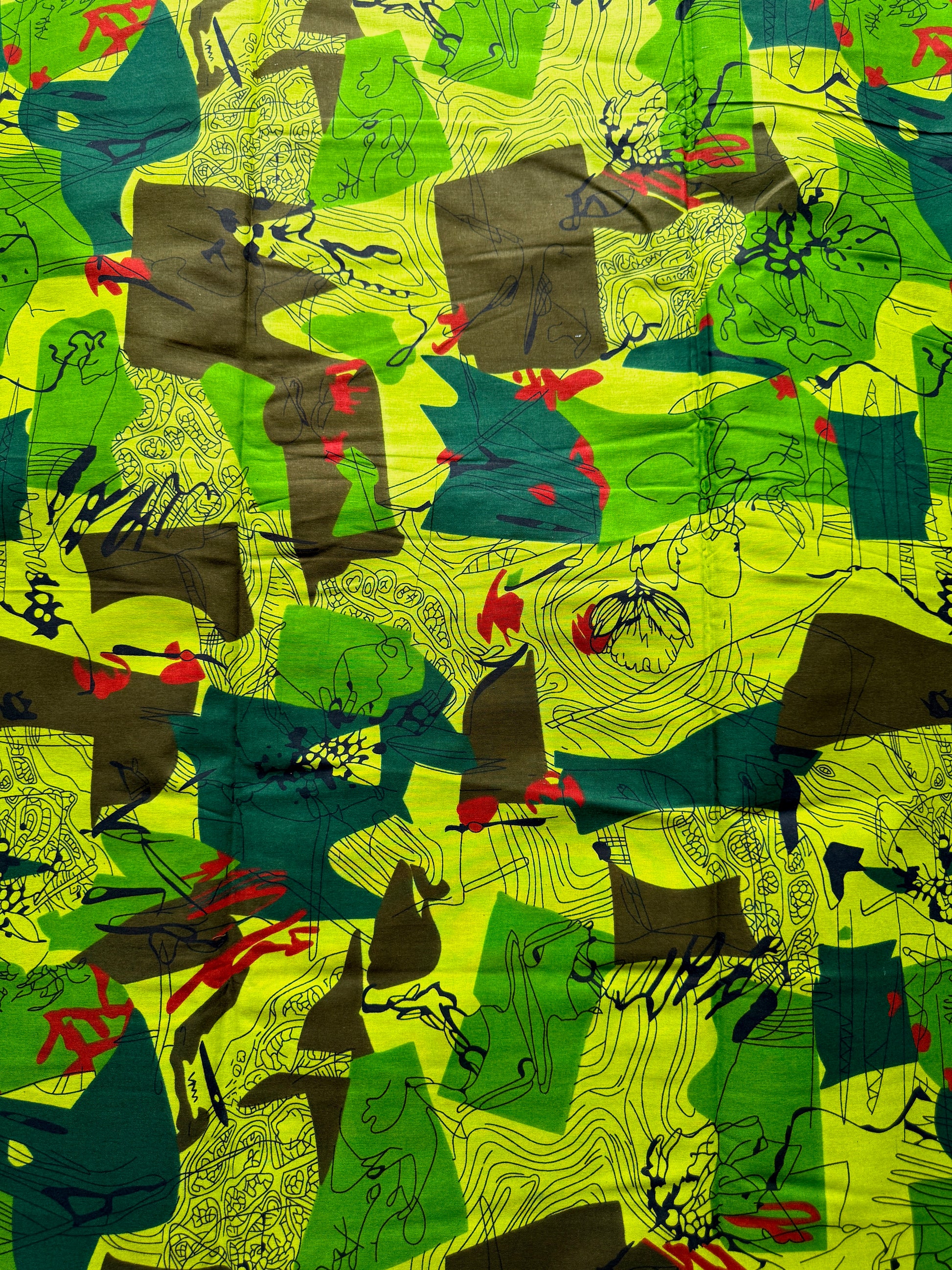 A close-up of a colorful abstract patterned fabric featuring bright lime green, forest green, dark teal, brown, black, and small red accents.