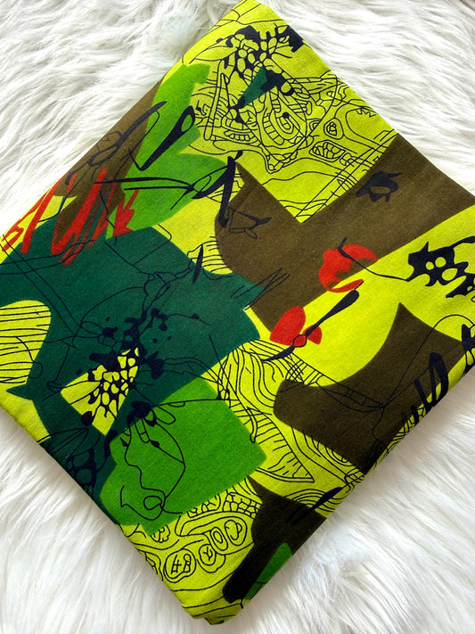 A folded square fabric item, likely a scarf or small bag, featuring an abstract multicolor print with lime green, forest green, brown, black, and red brushstrokes, displayed on a white faux fur surface.