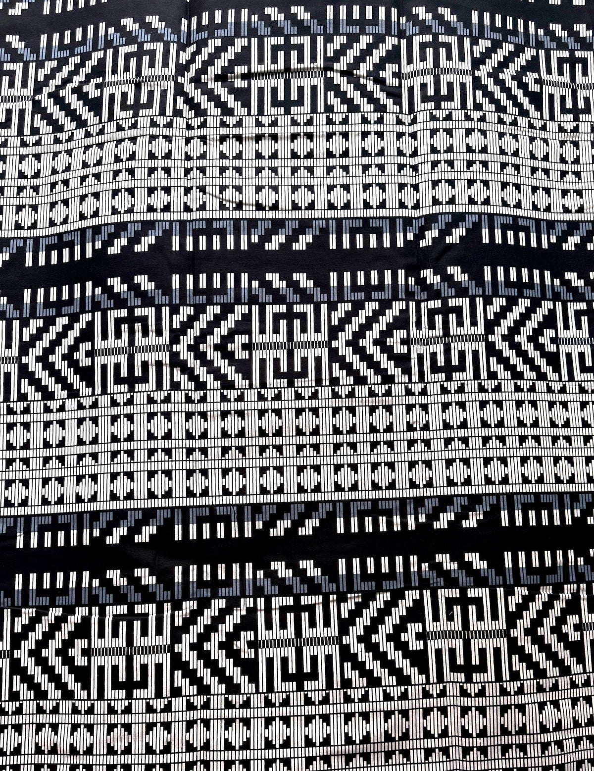 A close-up of a woven textile with horizontal bands of black and white geometric patterns, including zigzags, diamonds, and stepped motifs.