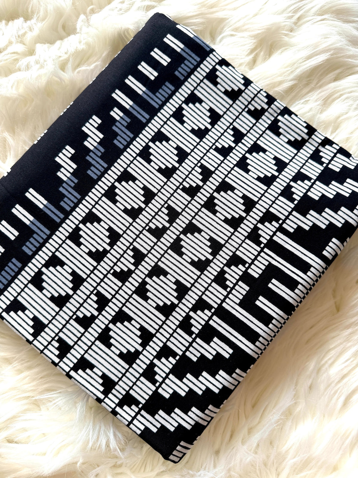 A folded black and white patterned blanket with a geometric ikat design, displayed on a fluffy white faux fur surface.