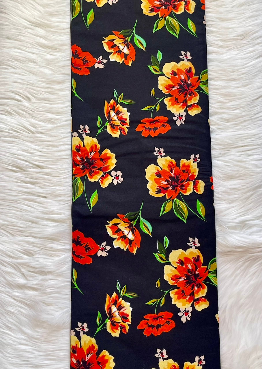 Floral-patterned fabric with orange and yellow flowers on a black background, laid flat on a white textured surface.