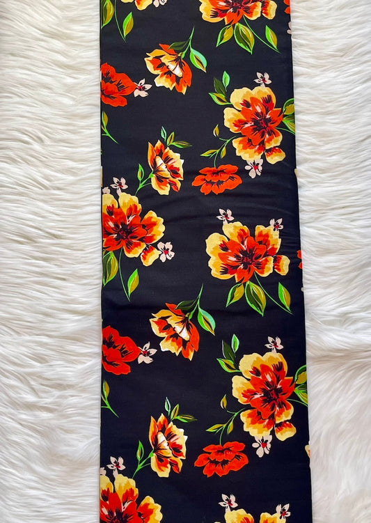 Floral-patterned fabric with orange and yellow flowers on a black background, laid flat on a white textured surface.