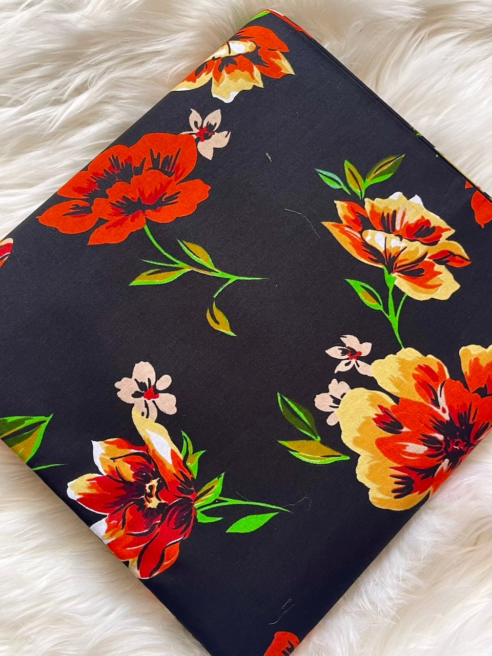 Floral-patterned fabric with red, orange, and yellow flowers on a black background, laid flat on a white surface.