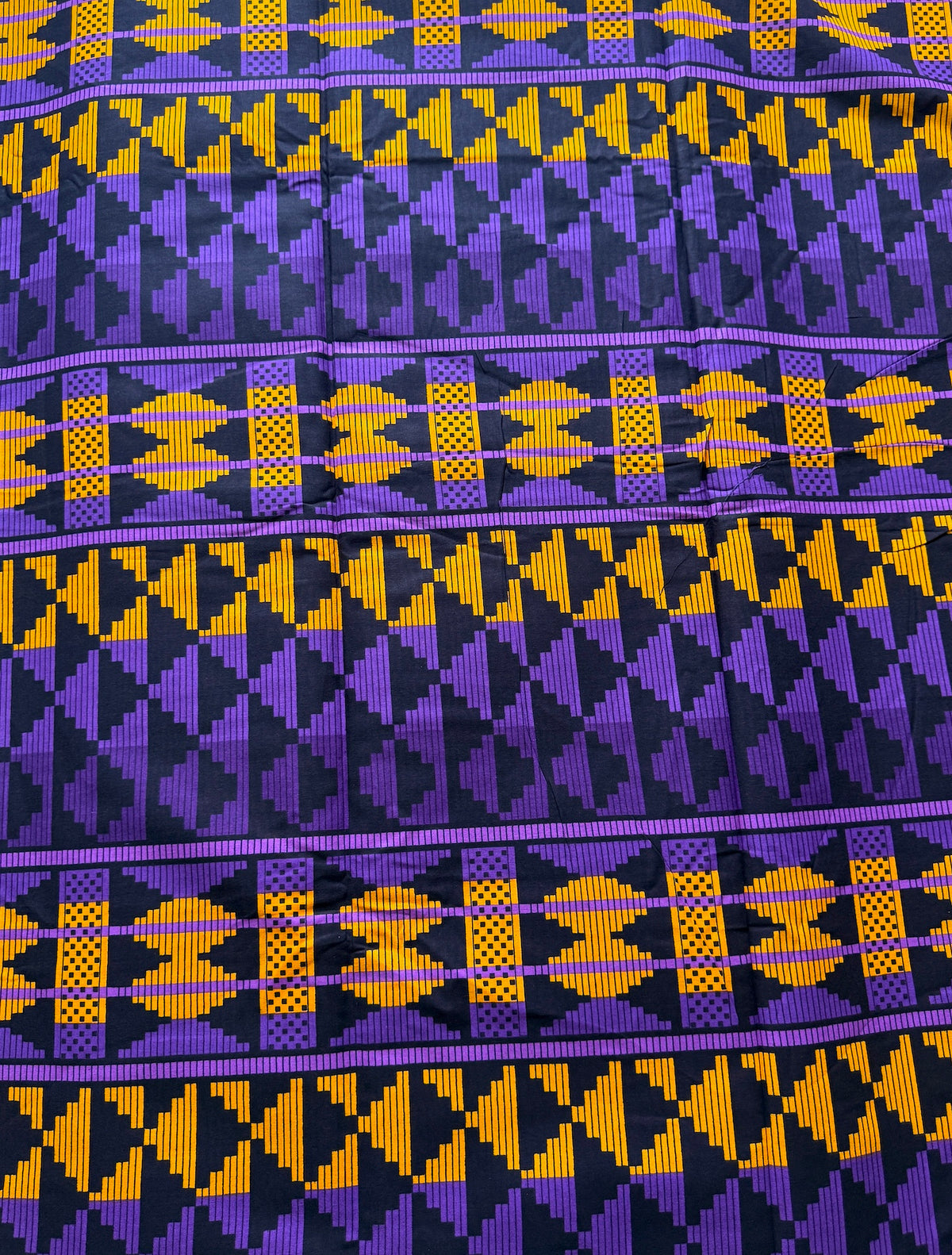 A close-up of a woven textile with a bold geometric pattern in purple, yellow, and black, showing horizontal bands of repeating tribal-style motifs.