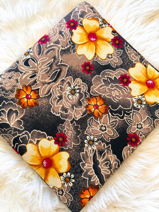 A square fabric item, likely a pillow cover or scarf, featuring a retro floral pattern with yellow, orange, and red flowers on a dark brown and beige background, displayed on a white faux fur surface.