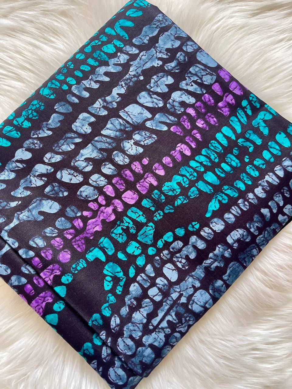 Folded fabric with blue and purple abstract pattern on a white fluffy surface