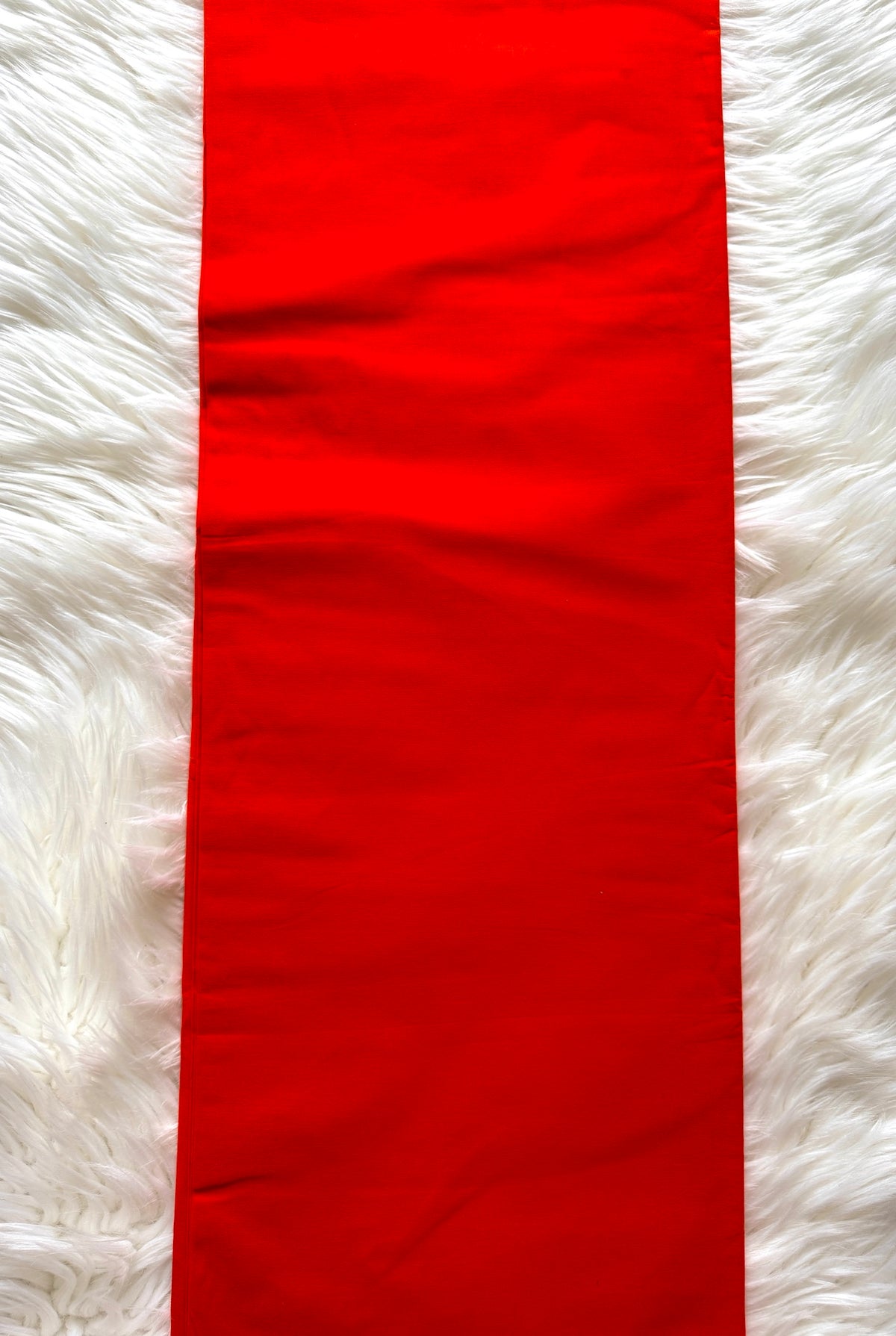 A bright red rectangular fabric runner or table runner laid flat on a white faux-fur surface.