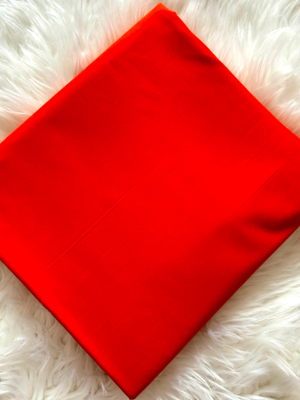 A bright red square fabric item, likely a pillowcase or folded textile, laid flat on a white faux fur surface.