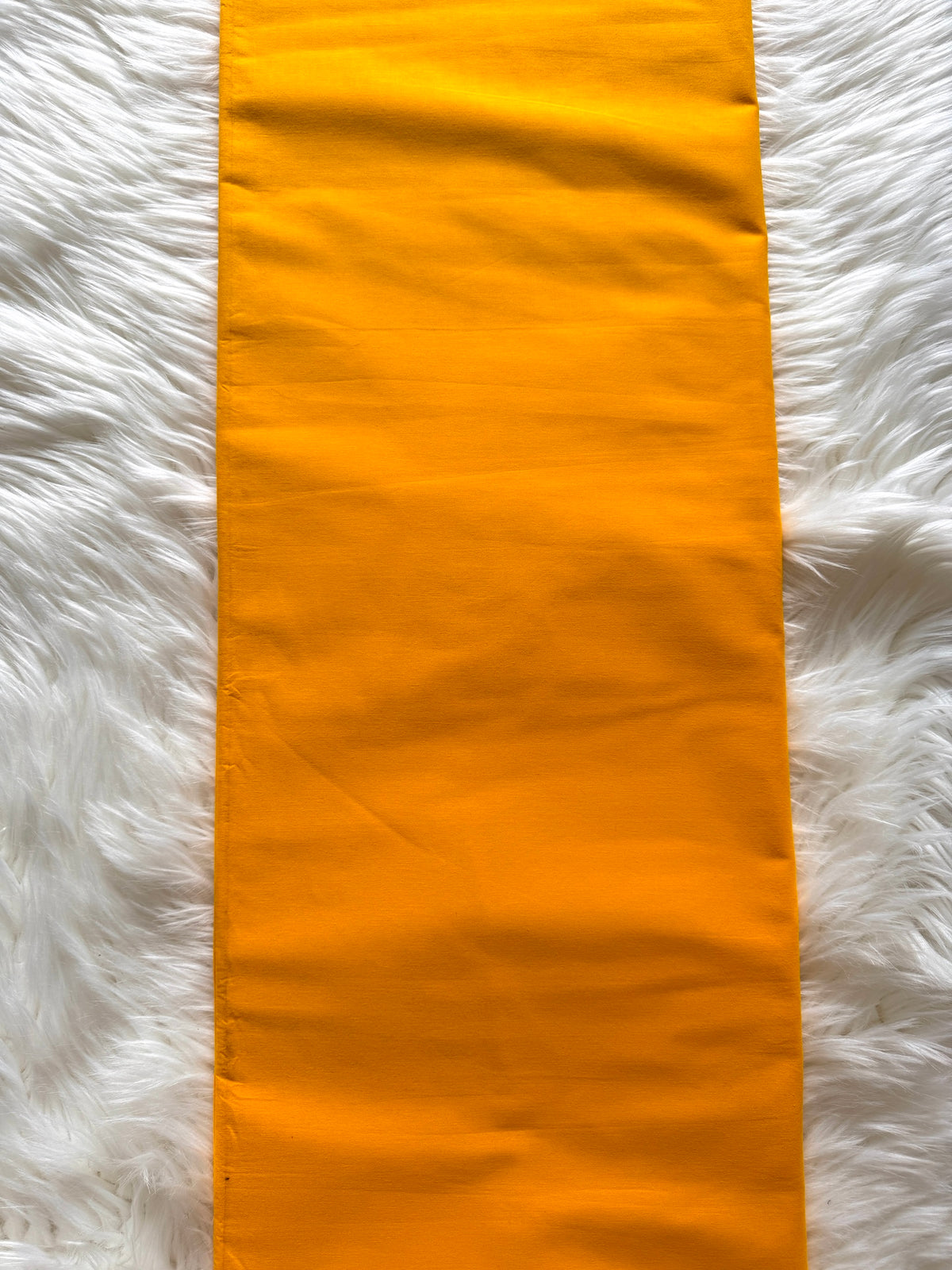 A bright orange fabric runner or table runner laid flat on a white faux fur surface.
