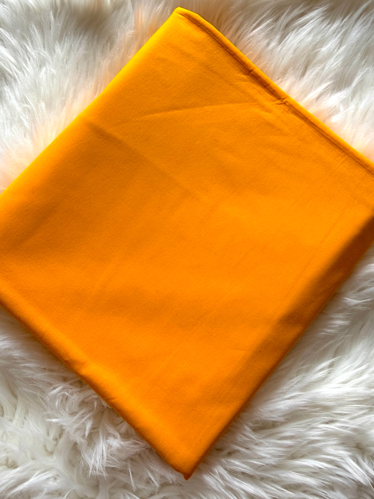 A folded bright orange fabric item, likely a blanket or throw, laid flat on a white faux fur surface.