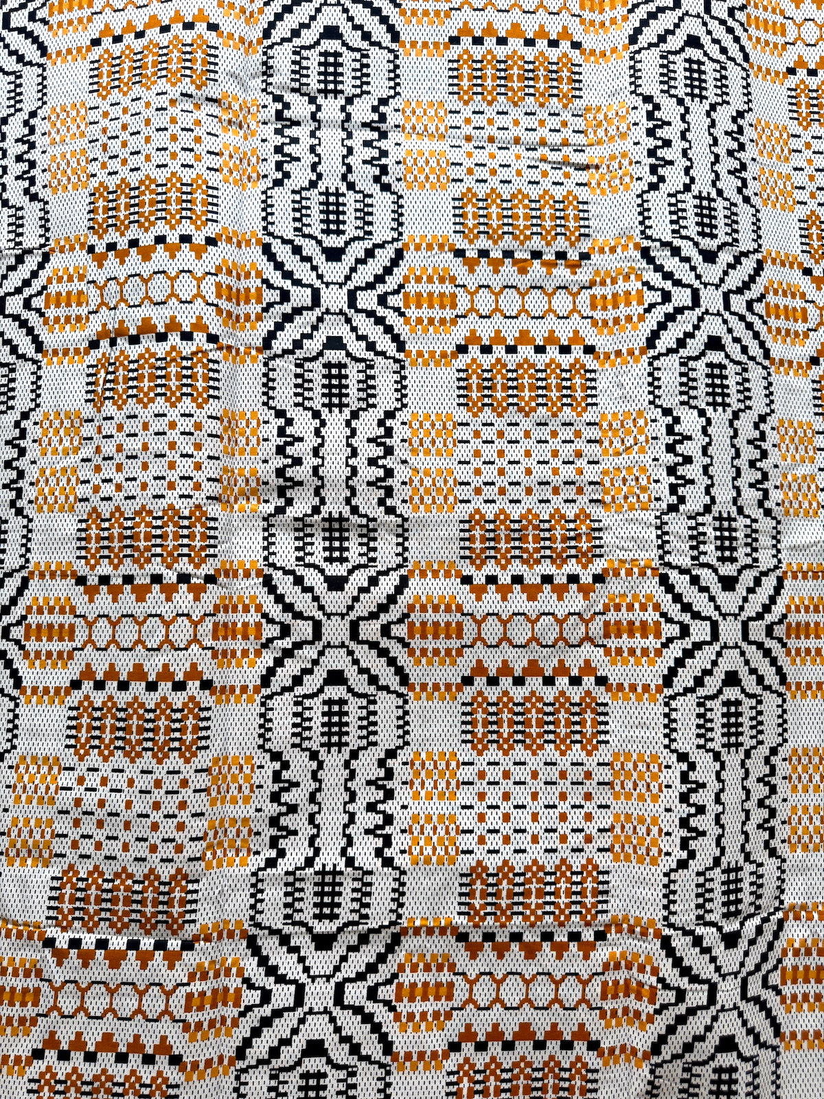 A close-up of a woven textile with a repeating geometric pattern in orange, black, and white.