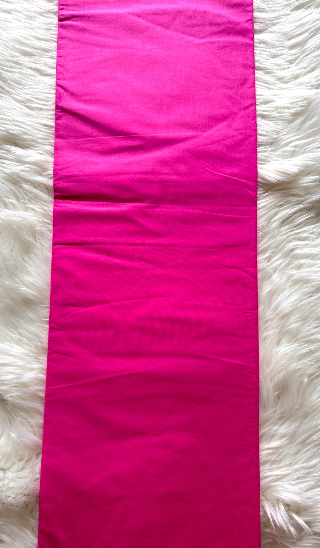 A bright hot pink fabric runner or table runner laid flat on a white faux fur surface.