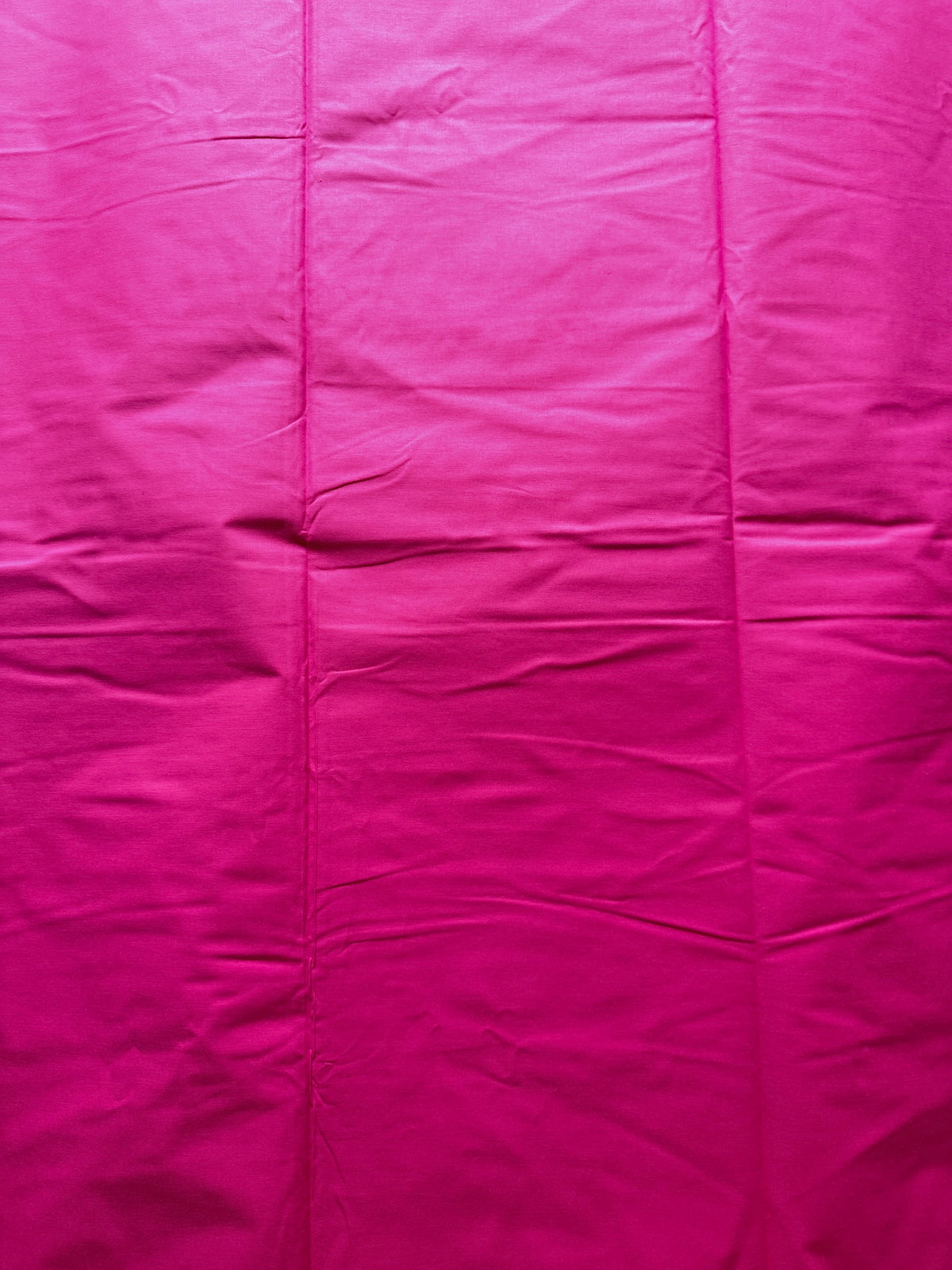 Bright pink fabric with visible folds and wrinkles, filling the entire frame.