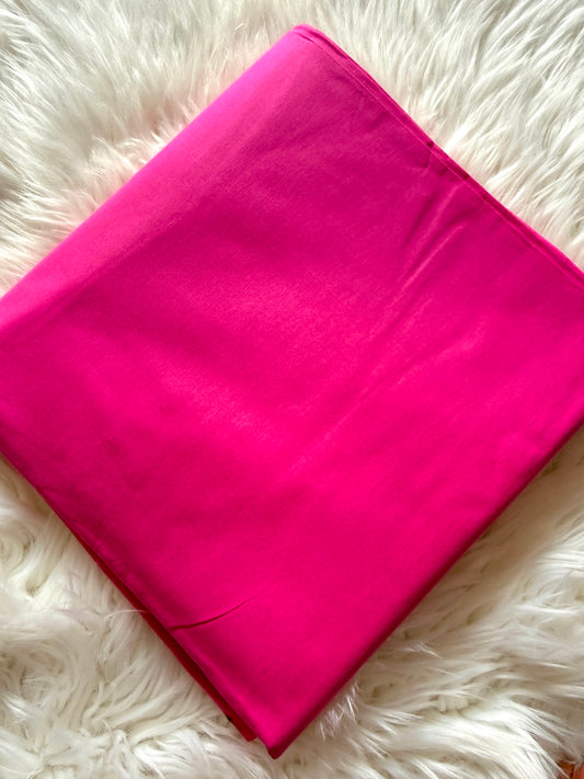 A folded piece of bright hot pink fabric, likely satin or silk, displayed diagonally on a white faux fur surface.