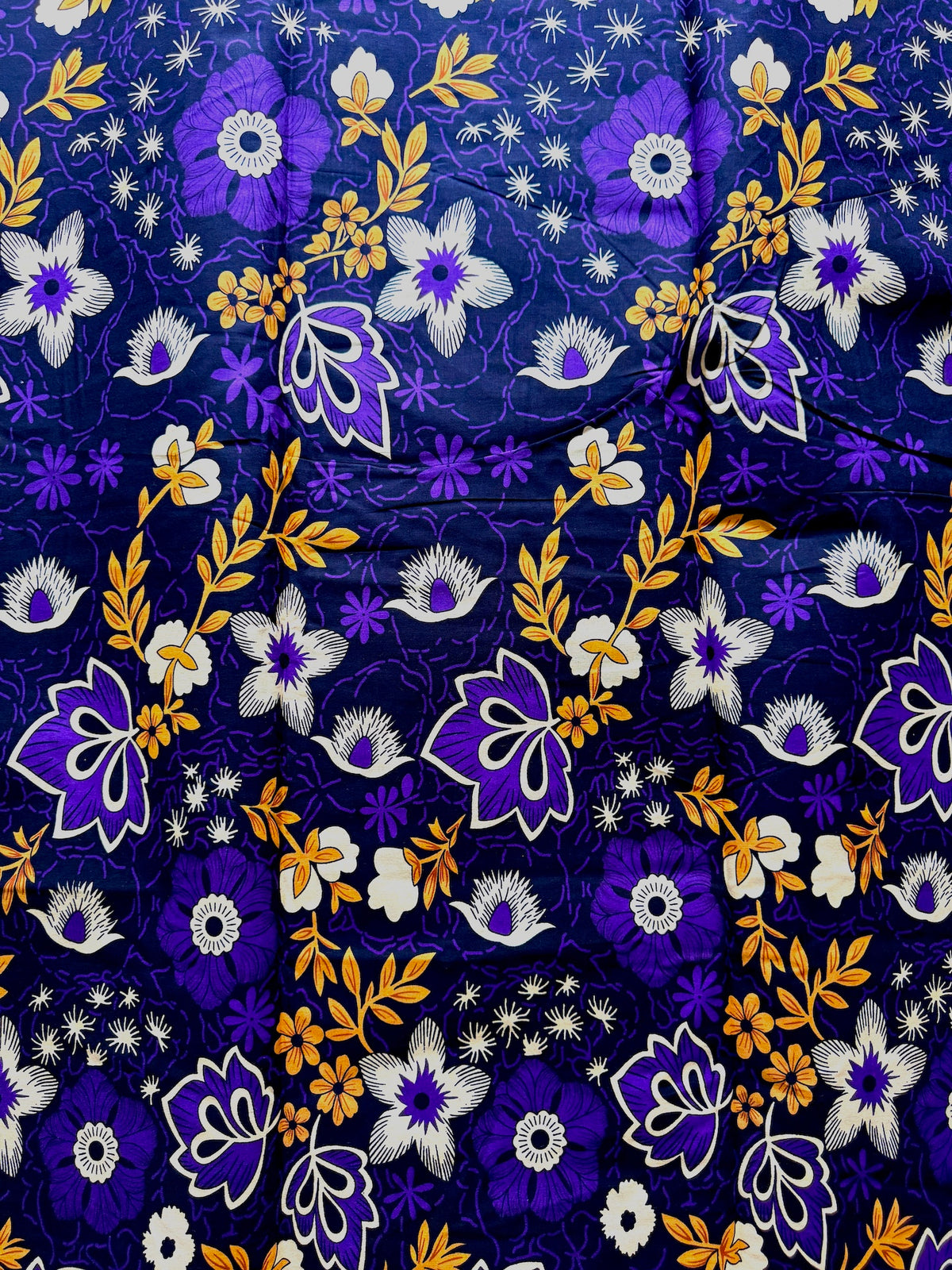 A close-up of a patterned fabric featuring a dense floral print with purple, white, and orange flowers on a dark navy blue background.
