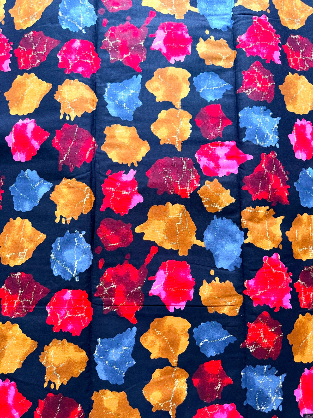 A close-up of a navy blue fabric with a colorful abstract watercolor-like print in pink, red, yellow, and blue.