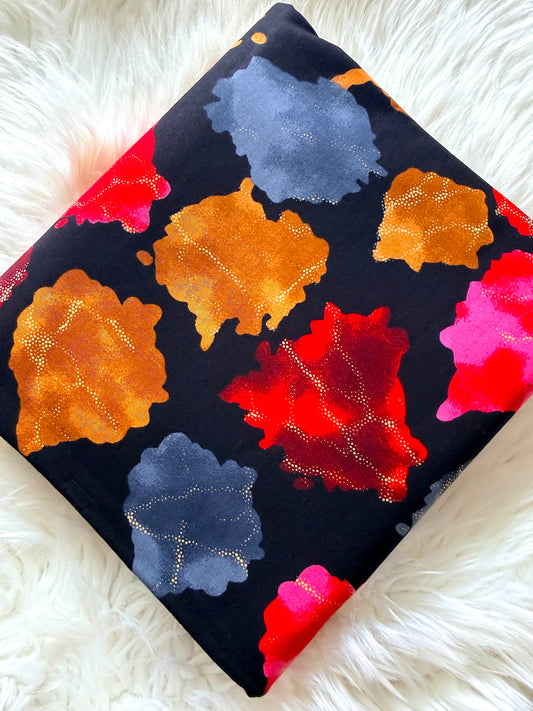 A square throw pillow with a black background and a colorful abstract floral pattern, resting on a white faux fur surface.