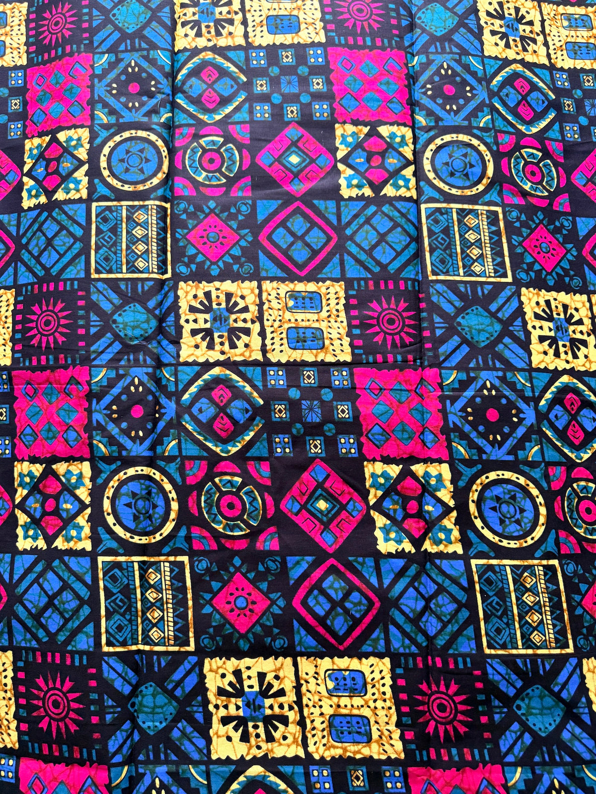 A close-up of a fabric with a vibrant, repeating patchwork-style geometric pattern in blue, magenta pink, yellow, and black.