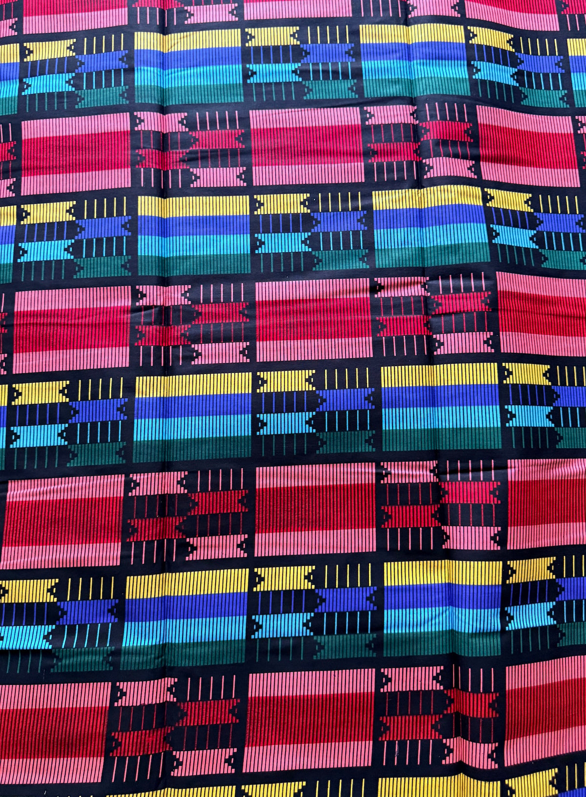 A close-up of a vibrant, multicolored woven fabric with a geometric pattern featuring stripes of pink, red, yellow, blue, and teal separated by black lines.