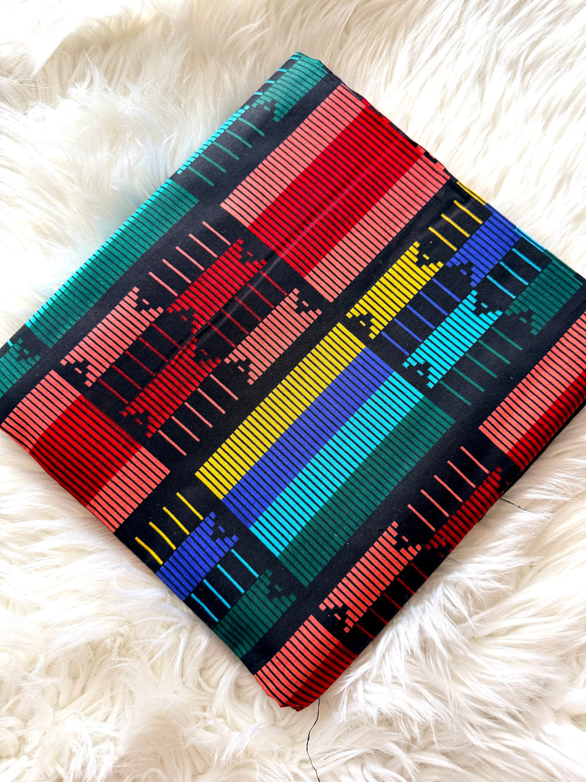 A square woven textile or pillow cover with a vibrant Southwestern geometric pattern, displayed diagonally on a white faux fur surface.