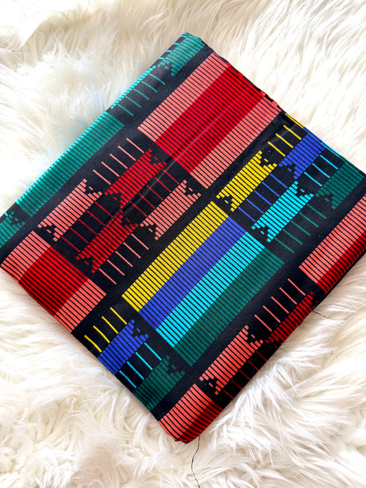 A square woven textile or pillow cover with a vibrant Southwestern geometric pattern, displayed diagonally on a white faux fur surface.