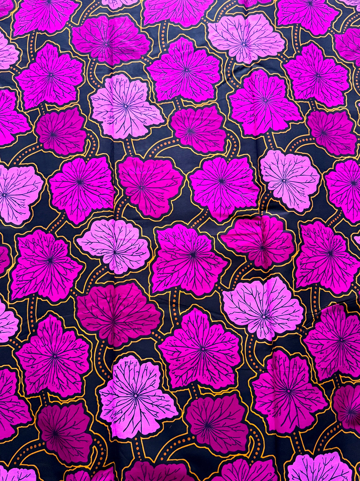 A close-up of a fabric pattern featuring bright magenta, pink, and purple hibiscus flowers with yellow outlines on a black background.
