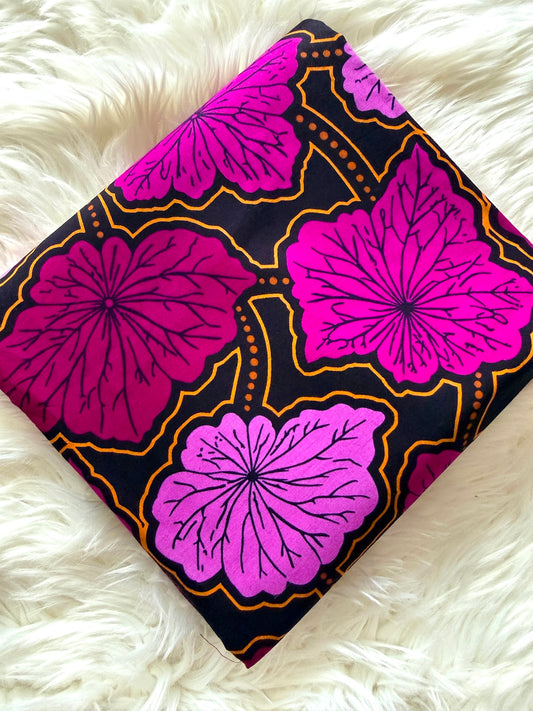 A square piece of dark patterned fabric with large pink and magenta floral motifs outlined in gold, laid flat on a white faux-fur surface.