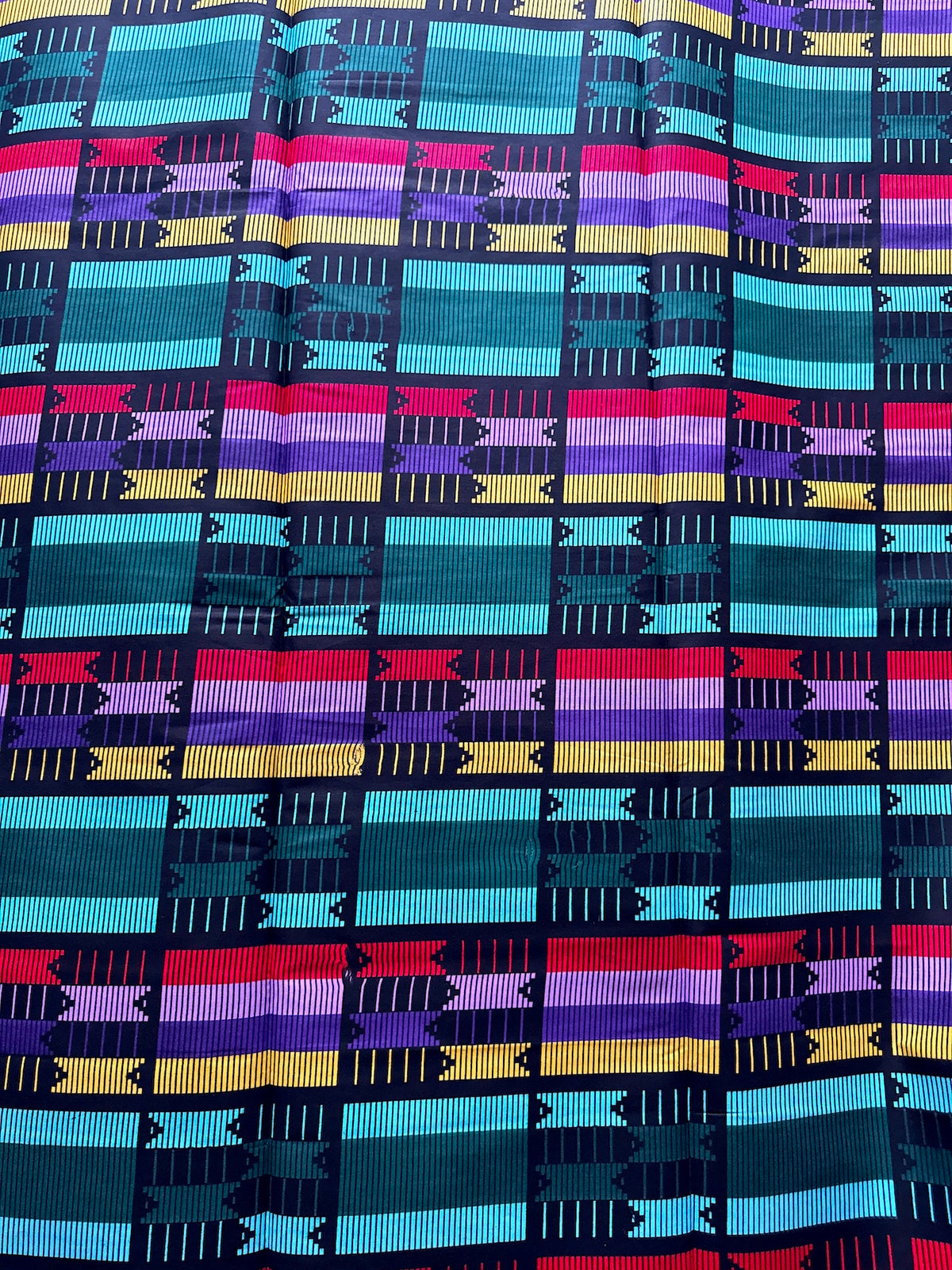 A close-up of a woven textile with a colorful geometric pattern featuring horizontal stripes in teal, turquoise, purple, pink, yellow, and red on a dark navy background.
