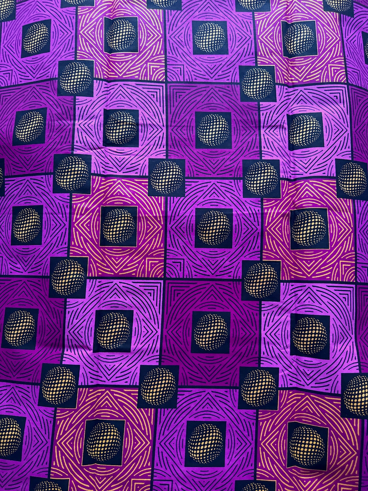 A close-up of a patterned fabric featuring a geometric design with purple, magenta, and pink squares, each containing a central black square with a gold 3D-effect mesh sphere.
