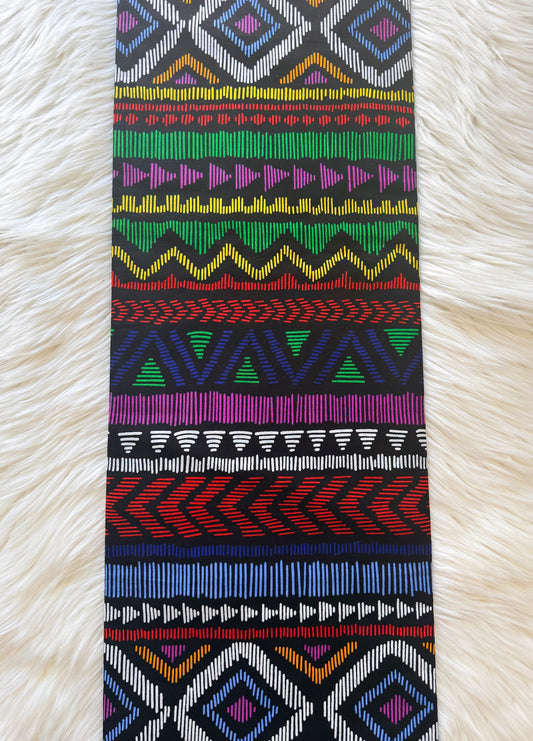 A long rectangular textile with a colorful geometric tribal pattern, laid flat on a white faux fur background.