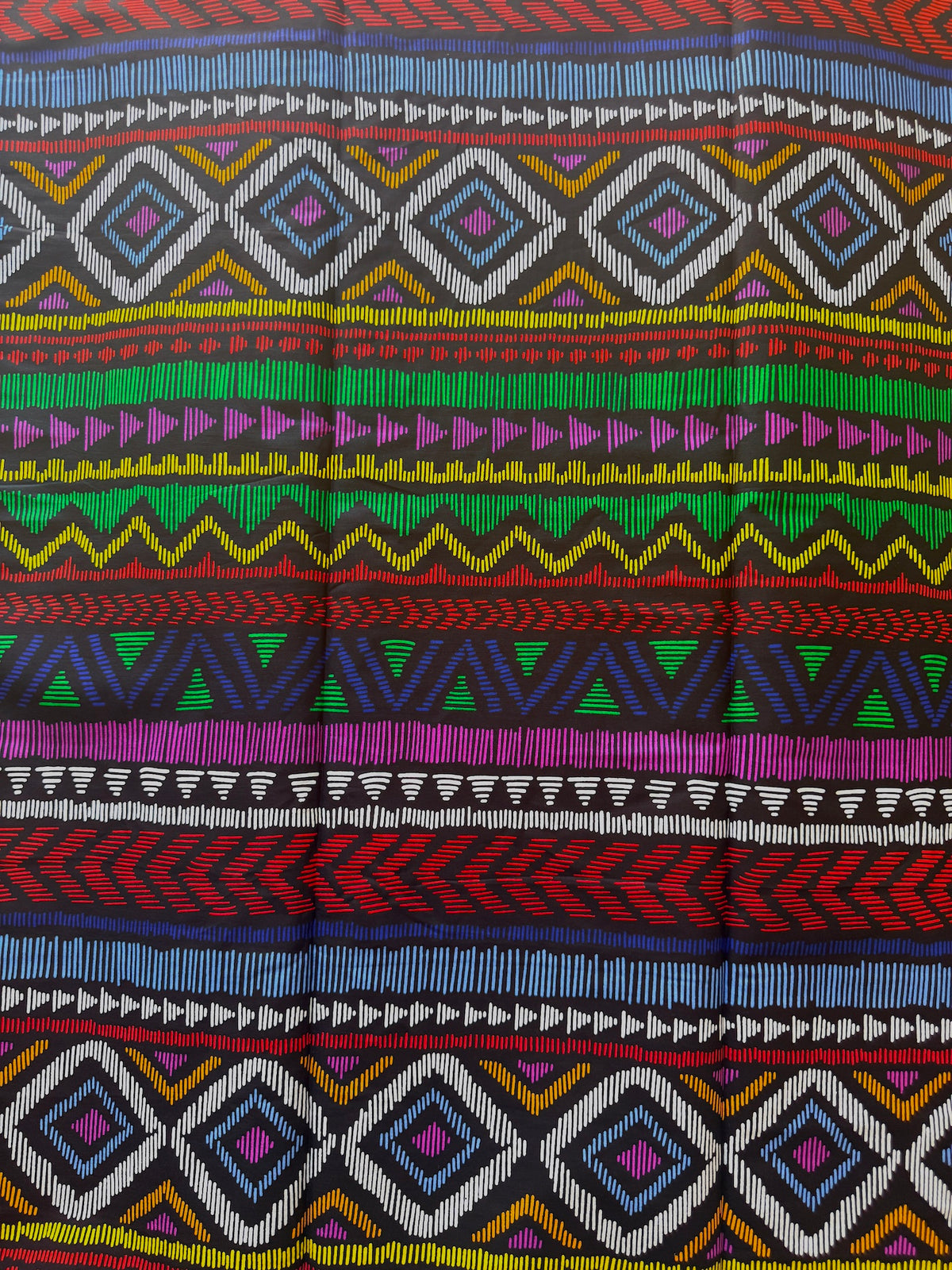 A close-up of a colorful woven textile with horizontal geometric bands including diamonds, triangles, zigzags, and stripes in red, blue, green, yellow, purple, black, and white.