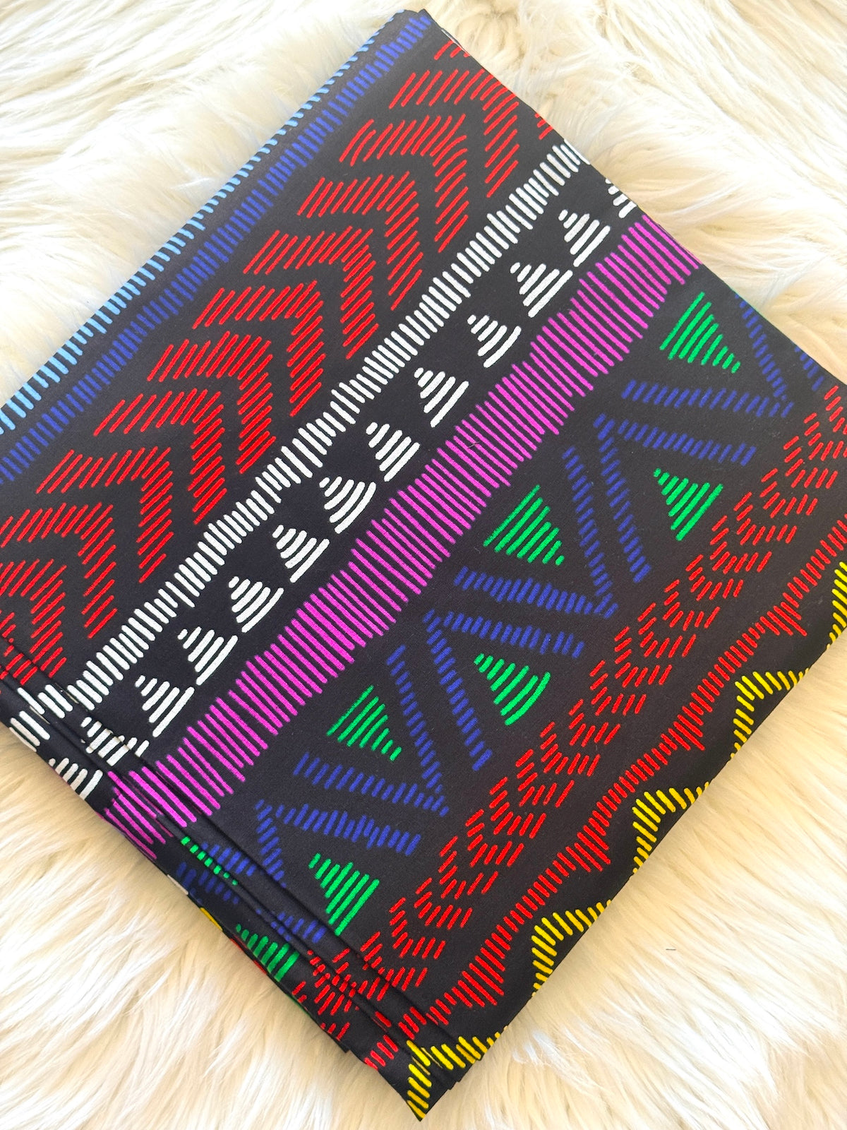 A square woven throw pillow with a vibrant multicolor geometric pattern, laid flat on a soft white faux fur surface.
