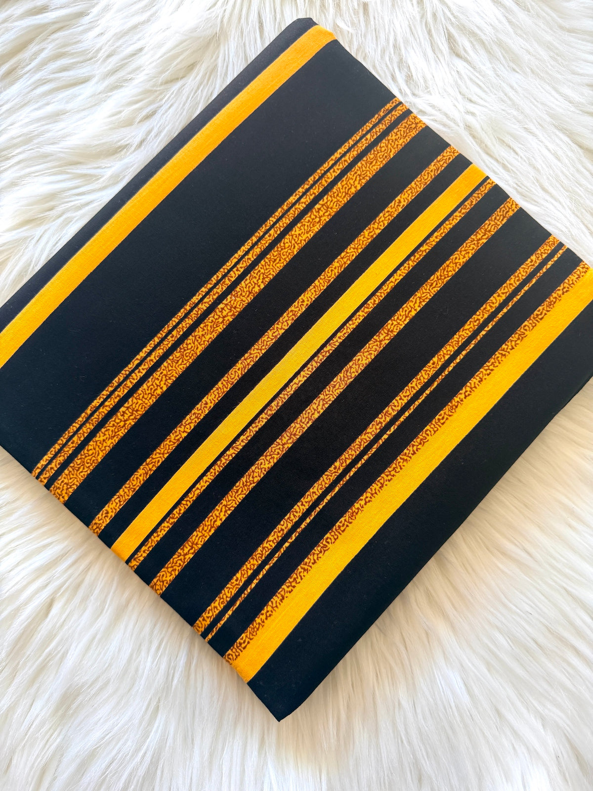 A square throw pillow with a black background and bold yellow stripes, laid flat on a white faux fur surface.