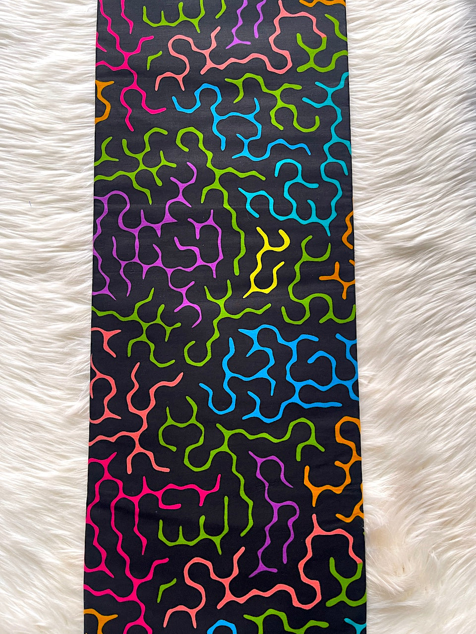 Colorful wavy patterned tie on a black background, placed on a white textured surface.
