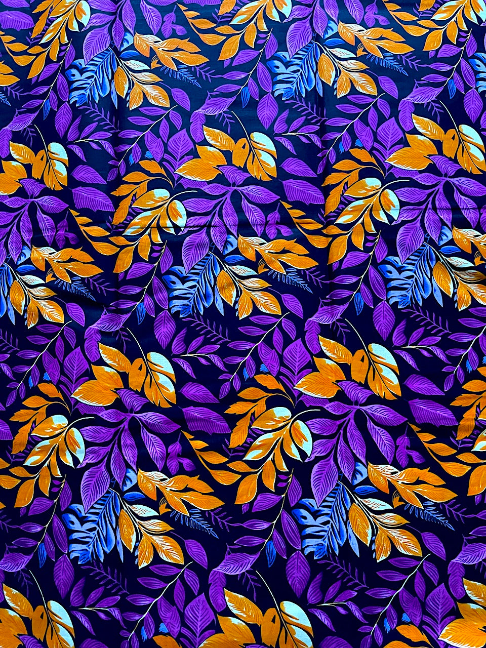 Patterned fabric with purple, orange, and blue leaves on a dark background